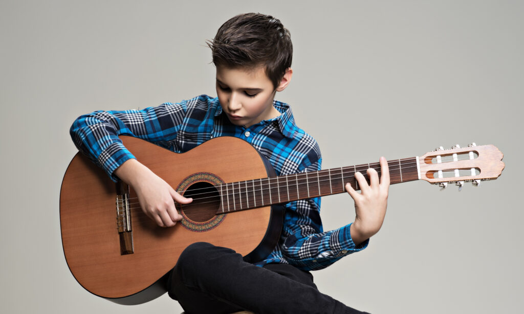 caucasian boy playing on acoustic guitar.