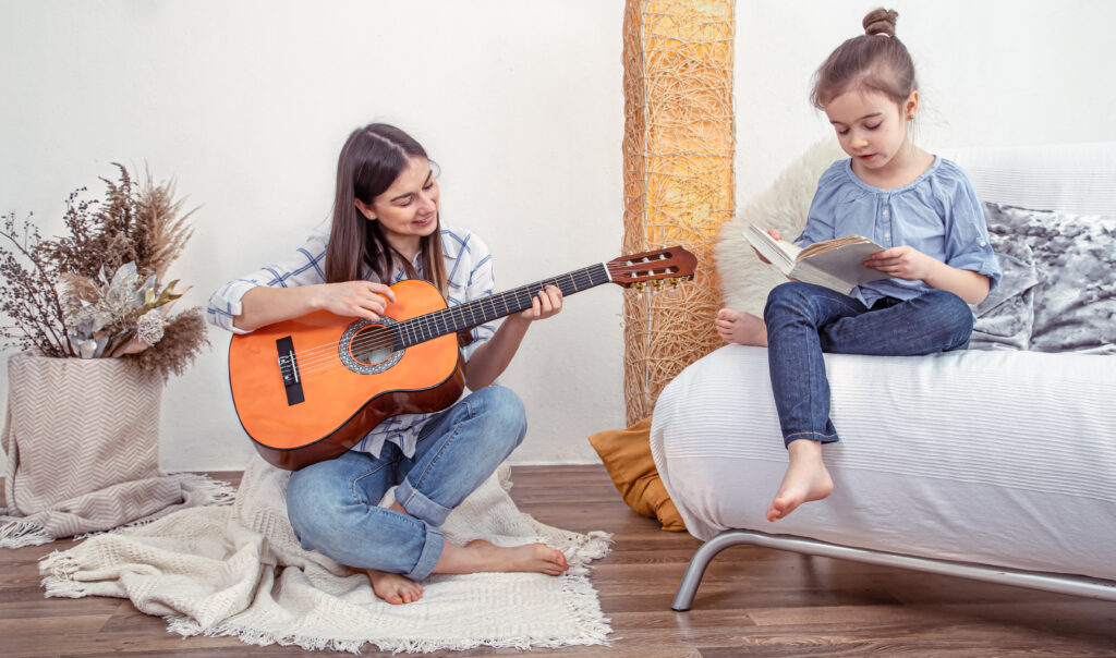 a young woman in the living room with a guitar playing for a child.